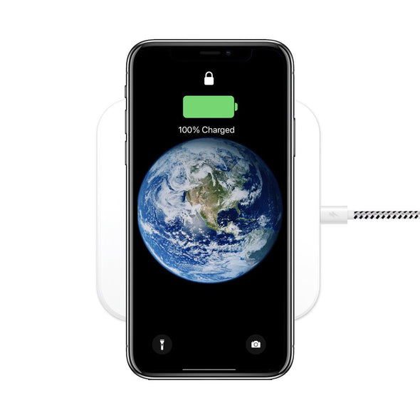 An iPhone with a display of the Earth is shown on a white wireless charging pad. The screen indicates it is 100% charged, with a green battery icon and a lock symbol at the top. A white cable is plugged into the pad.