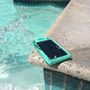 A Minty Fresh Solar Bank from ChargeCords, featuring quick charging capabilities, sits on the stone edge of a pool with water splashing onto it. The turquoise phone, equipped with a solar charging case and appearing to be waterproof, is partly submerged in the pool water.