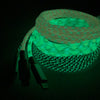 A stack of glowing braided cables in green light against a dark background. The ChargeCords Black and White Glow Lightning Cables (5 ft / 1.5m length) are wound in coils, with connectors visible at one end. The braided texture and vibrant glow, enhanced by reinforced aluminum shielding, create a striking visual contrast in the low-light setting.
