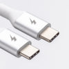 Close-up image of two ChargeCords Lime USB-C to USB-C Cables [6 ft / 1.8m length] with metallic connectors and lightning bolt symbols engraved on their surfaces, indicating they support fast charging and USB 3.1 speeds. The tangle-proof fabric ensures durability and ease of use with compatible devices. The cables are white, set against a smooth, light grey background.
